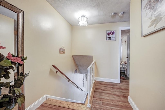 staircase featuring baseboards, a textured ceiling, and wood finished floors