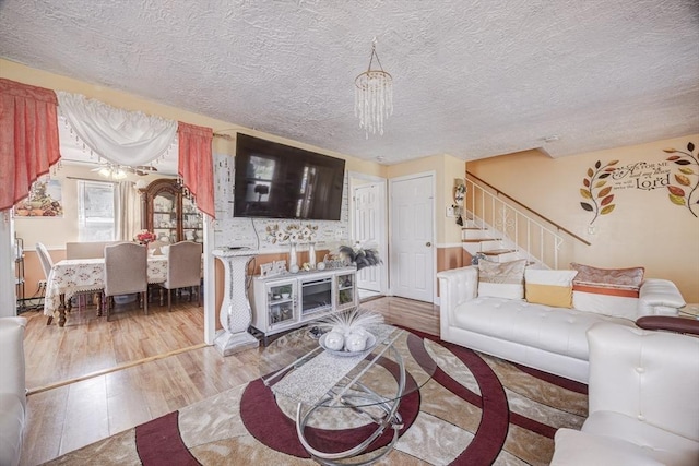 living room with a textured ceiling, stairs, wood finished floors, and a chandelier