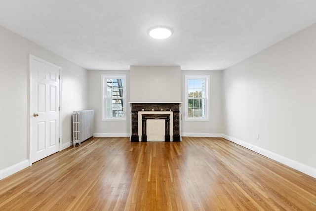 unfurnished living room featuring a fireplace, radiator, and light hardwood / wood-style flooring