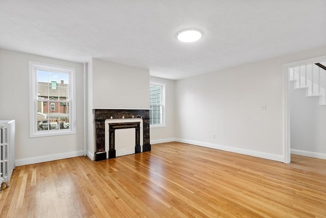 unfurnished living room with light hardwood / wood-style floors, a high end fireplace, and radiator