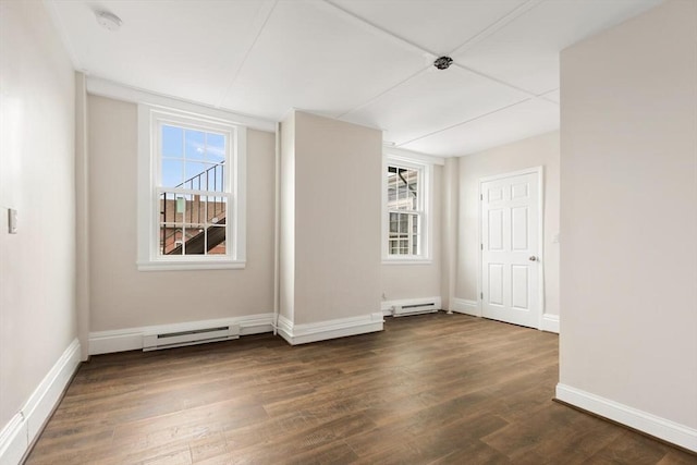 spare room featuring baseboard heating, dark wood-type flooring, and a healthy amount of sunlight