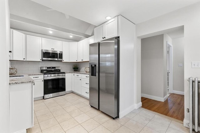 kitchen featuring light stone countertops, light tile patterned floors, decorative backsplash, white cabinetry, and appliances with stainless steel finishes