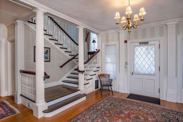 entryway featuring crown molding, light hardwood / wood-style floors, a chandelier, and ornate columns