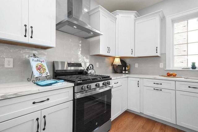 117 Montvale Ave, Woburn, MA 01801 - kitchen featuring stainless steel range with gas cooktop, wall chimney exhaust hood, white cabinets, light wood-style flooring, and decorative backsplash