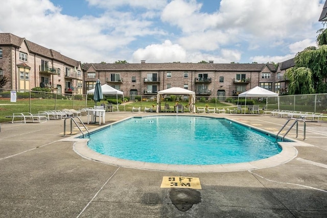 community pool with a gazebo, fence, and a patio area