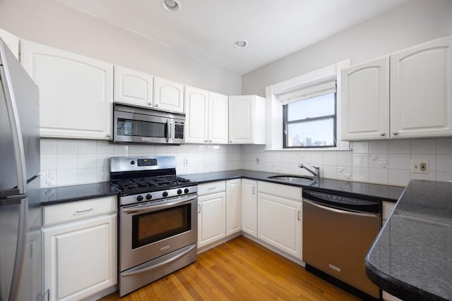 kitchen with appliances with stainless steel finishes, white cabinetry, sink, decorative backsplash, and light wood-type flooring