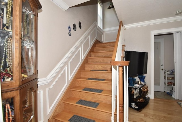 stairs with a decorative wall, ornamental molding, wainscoting, and wood finished floors