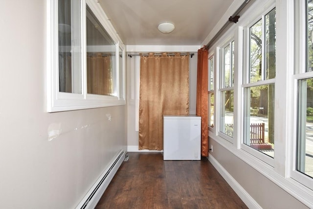 unfurnished sunroom featuring wood finished floors, healthy amount of natural light, baseboards, and a baseboard radiator