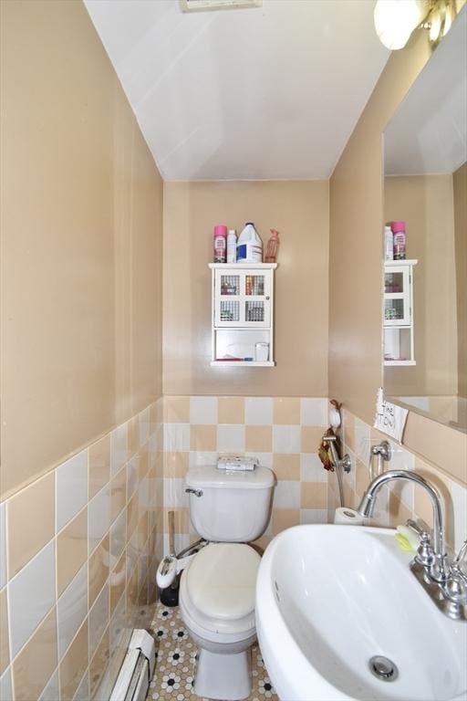 half bathroom featuring a sink, tile walls, toilet, and wainscoting
