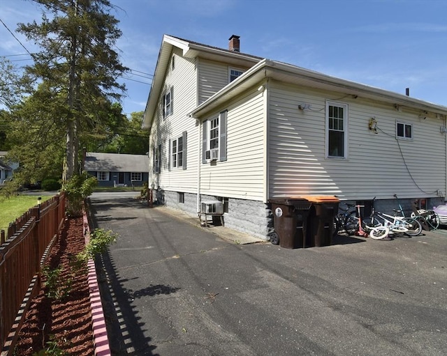 view of side of home with fence, a chimney, and driveway