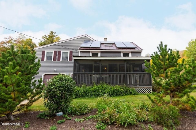 rear view of property featuring a garage, a sunroom, and solar panels