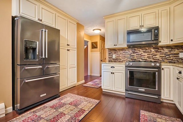 kitchen featuring dark hardwood / wood-style floors, decorative backsplash, light stone countertops, cream cabinetry, and stainless steel appliances