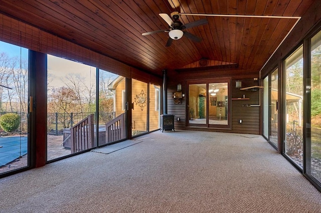 unfurnished sunroom with lofted ceiling, a wood stove, ceiling fan, and wooden ceiling