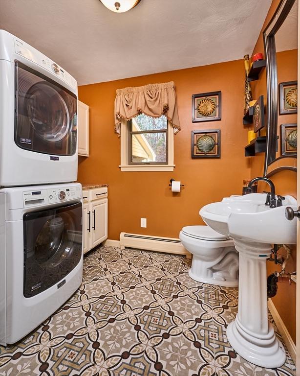 washroom with a baseboard radiator and stacked washer / dryer