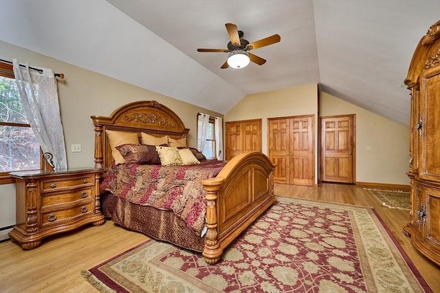 bedroom featuring vaulted ceiling, light hardwood / wood-style flooring, ceiling fan, and multiple closets