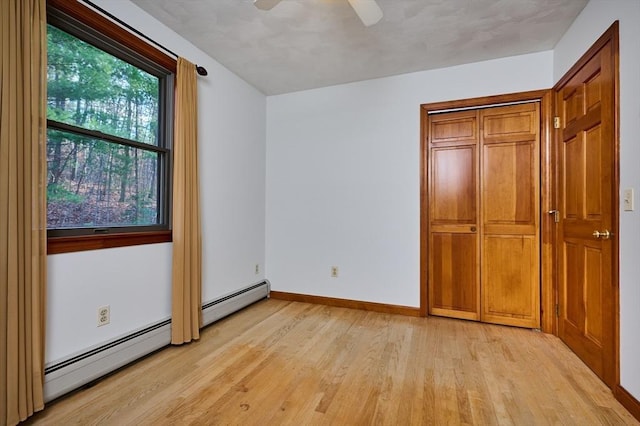 unfurnished bedroom with ceiling fan, light hardwood / wood-style flooring, and a baseboard heating unit