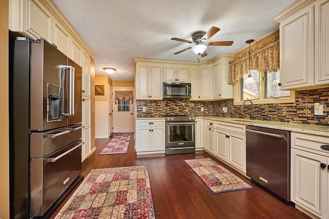 kitchen featuring appliances with stainless steel finishes, pendant lighting, dark wood-type flooring, and cream cabinets