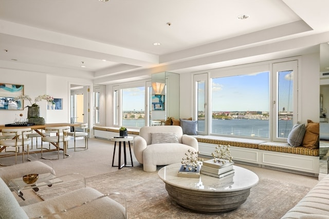 living room featuring a raised ceiling, a water view, and light colored carpet