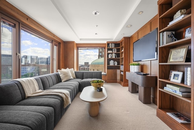 carpeted living room featuring a raised ceiling and wooden walls