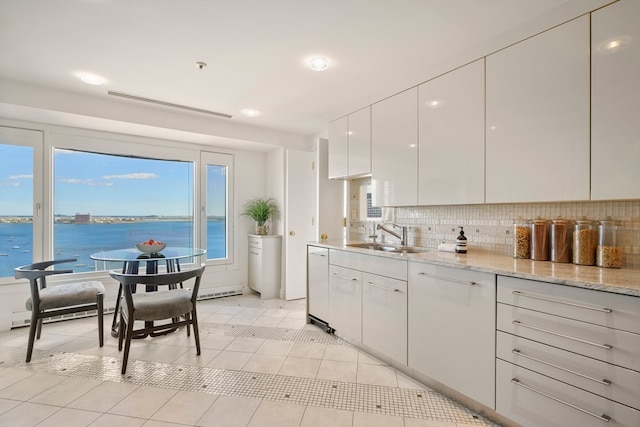 kitchen featuring tasteful backsplash, sink, white cabinetry, a water view, and light tile patterned floors