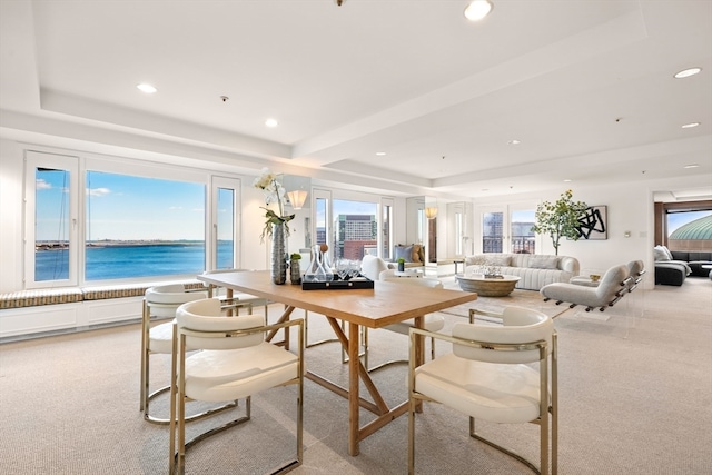 dining room featuring light carpet, a water view, and a raised ceiling