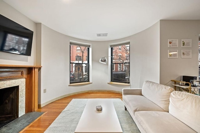 living room with light wood-style flooring, visible vents, baseboards, and a fireplace with flush hearth