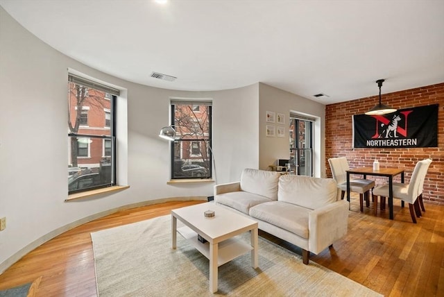 living area with visible vents, brick wall, light wood-style flooring, and baseboards