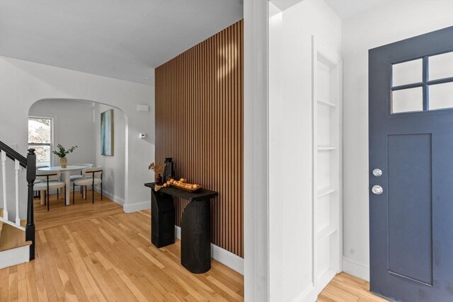 foyer entrance with arched walkways, stairway, light wood finished floors, and baseboards