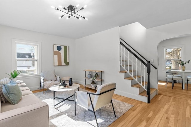 living room featuring an inviting chandelier, stairs, light wood-type flooring, and a wealth of natural light