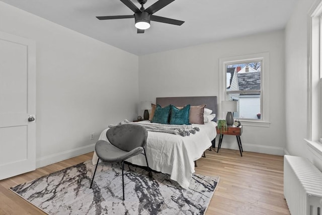 bedroom featuring light wood-style flooring, baseboards, ceiling fan, and radiator