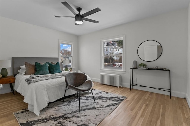 bedroom with radiator heating unit, multiple windows, and light wood-style flooring