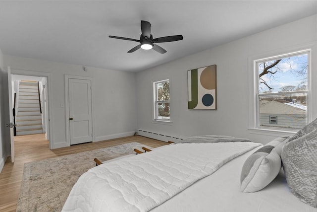 bedroom with a baseboard heating unit, baseboards, a ceiling fan, and light wood-type flooring