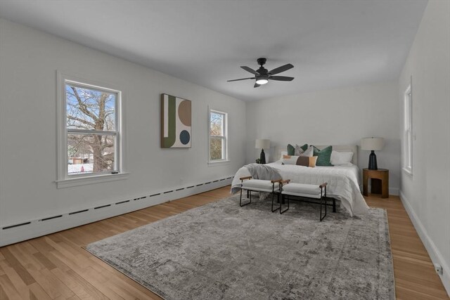 bedroom with baseboard heating, ceiling fan, baseboards, and light wood-style floors