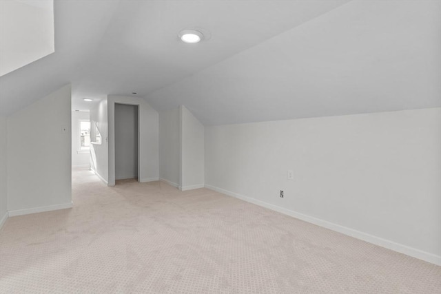 additional living space featuring baseboards, vaulted ceiling, and light colored carpet