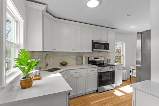 kitchen featuring white cabinets, a sink, radiator, tasteful backsplash, and appliances with stainless steel finishes