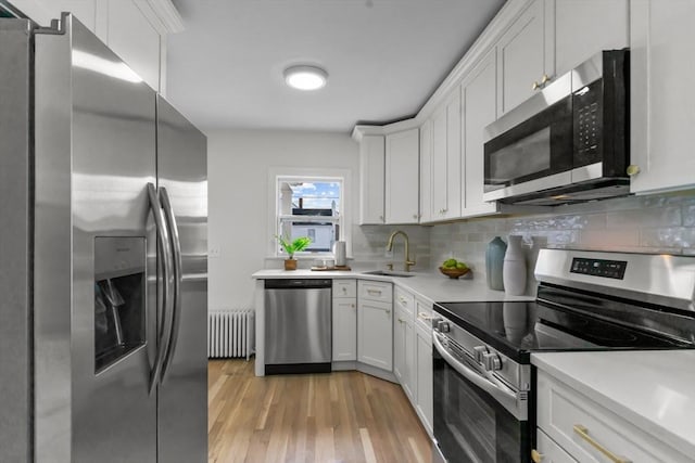kitchen with radiator heating unit, a sink, light countertops, light wood-style flooring, and appliances with stainless steel finishes