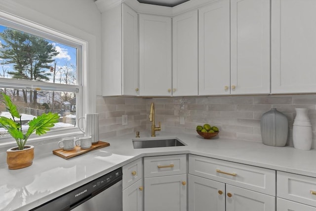 kitchen featuring white cabinets, light countertops, stainless steel dishwasher, a sink, and tasteful backsplash