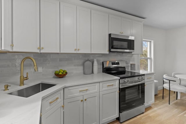 kitchen featuring stainless steel appliances, a sink, white cabinetry, and tasteful backsplash
