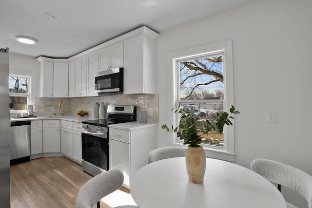 kitchen with light wood-style flooring, light countertops, backsplash, and appliances with stainless steel finishes