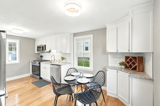 132 Nelson St, West Springfield, MA 01089 - kitchen featuring appliances with stainless steel finishes, light wood finished floors, white cabinetry, and backsplash
