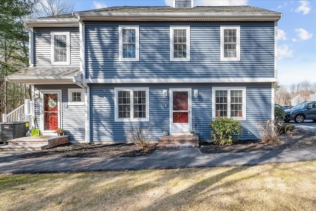 colonial inspired home with central AC unit, a chimney, and entry steps