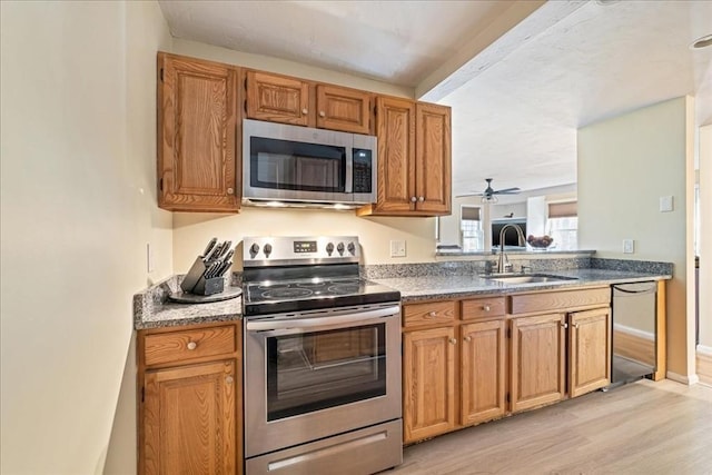 kitchen with light wood-style flooring, a sink, stainless steel appliances, brown cabinetry, and baseboards