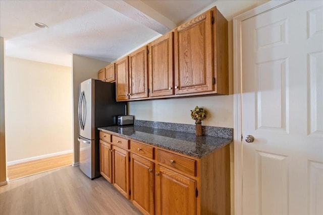 kitchen with dark stone countertops, brown cabinetry, light wood-type flooring, and freestanding refrigerator