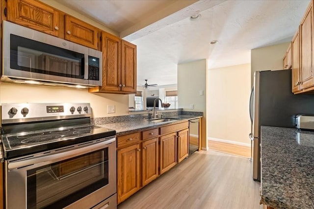 kitchen featuring baseboards, light wood-style flooring, a sink, appliances with stainless steel finishes, and brown cabinets