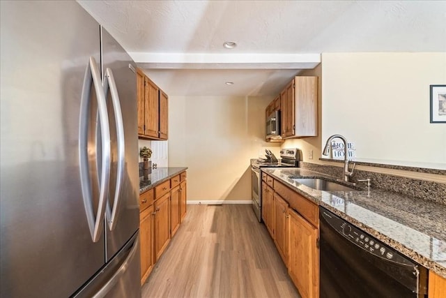 kitchen featuring brown cabinetry, light wood-type flooring, appliances with stainless steel finishes, and a sink