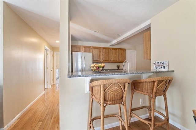 kitchen featuring brown cabinetry, baseboards, light wood finished floors, freestanding refrigerator, and a kitchen breakfast bar