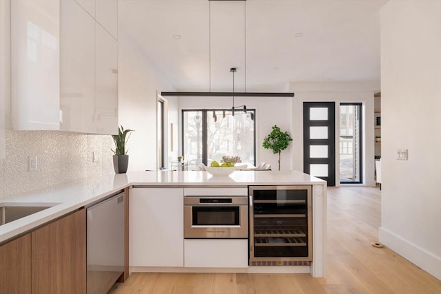 kitchen featuring appliances with stainless steel finishes, backsplash, white cabinets, wine cooler, and hanging light fixtures