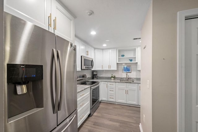 42 2nd Ave Unit 40, North Attleboro, MA 02760 - kitchen featuring appliances with stainless steel finishes, open shelves, white cabinetry, wood finished floors, and tasteful backsplash