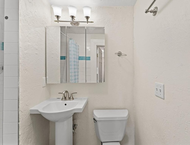 bathroom featuring a shower with curtain, toilet, and a textured wall