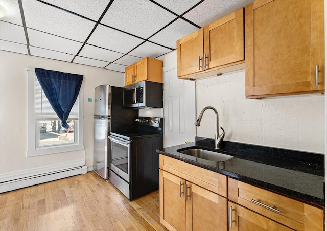 kitchen with light wood-type flooring, dark stone counters, a drop ceiling, a sink, and appliances with stainless steel finishes
